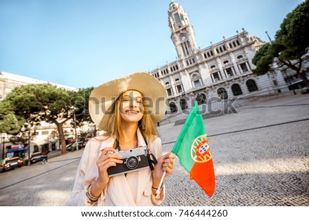 Portrait of a young woman tourist in sunhat standing with portuguese flag in front of the city hall building during the morning light in Porto, Portugal