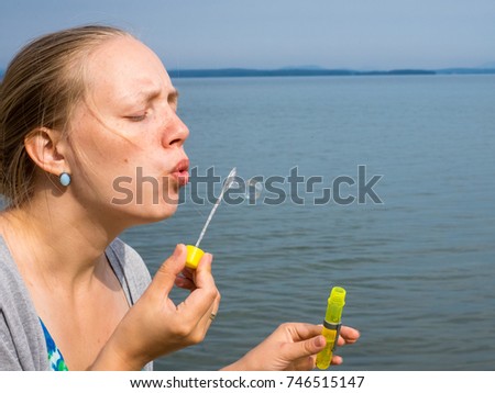 Close up side view shot of young female model blowing soap bubbles on beautiful sea and beach background.