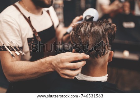 Close-up, master Barber does the hairstyle and styling with dryer, dries hair to guy. Concept Barbershop. Soft focus. Royalty-Free Stock Photo #746531563