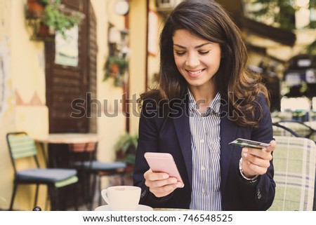 Smiling young woman using smart phone to check a credit card. 