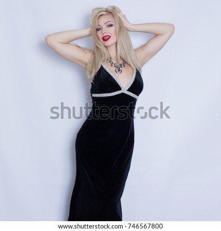 Beautiful blonde woman in black evening dress posing on grey background. Girl with black necklace 