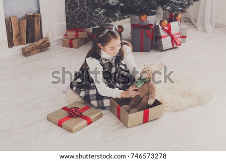Cute happy girl play with toy rabbit, christmas present on holiday morning in beautiful room. Female child got Xmas gift near decorated fir tree and fireplace. Winter holidays concept