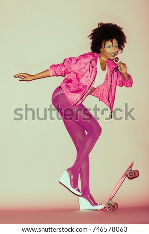 african american 80s girl in pink clothes posing with penny board and lollipop  