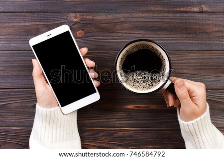 Close up business man's hand holds smart phone with black isolated screen over wooden background and coffee.
