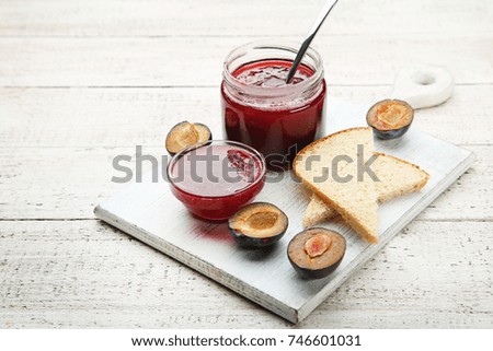 Plum jam in jar with bread on white wooden table
