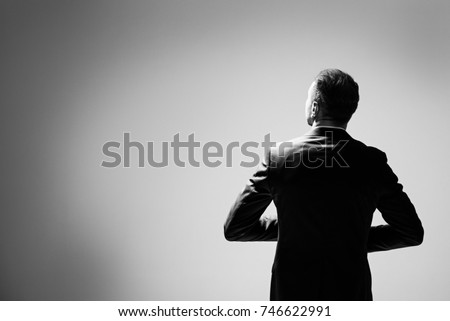 Corporate business male in modern suit standing in large empty gray space concept. man walking with confidence. Rear view. A man keeps his arms bent, his gaze is directed upwards to the right.