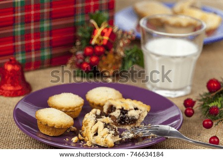 Broken mince pie on a purple plate with a glass of milk on a christmas table with a hessian tablecloth