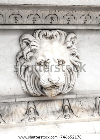 Close up photograph of detailed vintage lion head fountain carving in marble in Paris France with spigot coming out of its mouth and ornamental carved mouldings above and below
