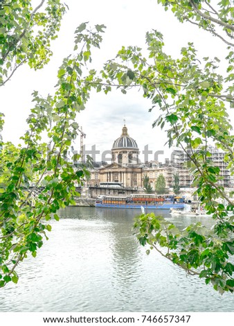 Beautiful tree branch framed photograph of the historic Institut de France building with baroque architectural detailing and large cupola topped dome at the end of Pont des Arts bridge in Paris France