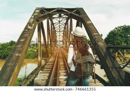 Traveler woman with backpack walking on railroad and take photo the old iron bridge, Travel in Thailand, Summer and vacation trip