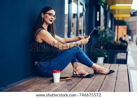 Attractive pondering brunette in cool spectacles thinking about feedback for publication in website while sitting outside.Charming pensive female spending leisure time next to copy space wall