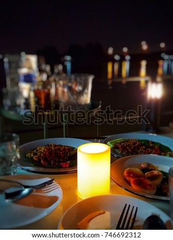 Electric candle on the dinner table. Night view of the Chao Phraya River at waterfront restaurant. Blur background, Focus selected Royalty-Free Stock Photo #746692312