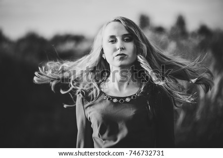 Portrait of a beautiful girl stand  in autumn in a red dress against the background of the field on the nature. upper half. look straight ahead. Close up. Black and white photo.