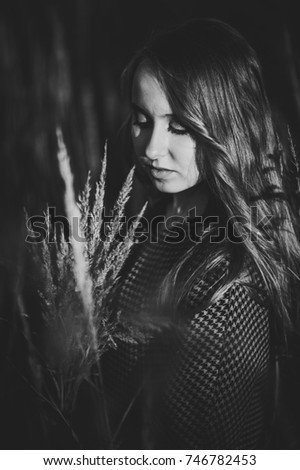 Portrait of girl with a bouquet of dried grass in autumn in a tall long grass the background of the field on the nature. upper half length. Close up. looking down. closed eyes. Black and white photo.