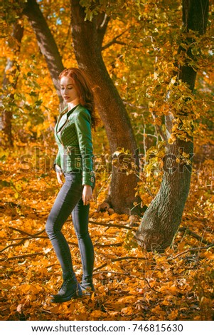 Beautiful and nice red-haired lady, looks stylish, dressed in a green leather jacket and black jeans.