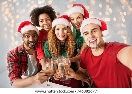 christmas, celebration and holidays concept - happy friends in santa hats clinking glasses of non-alcoholic sparkling wine at home party over lights background