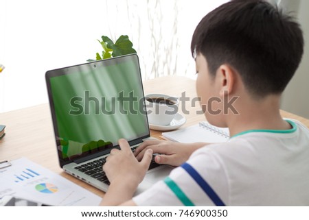 Over the shoulder shot of an Asain boy typing on a computer laptop with a key-green screen. Asian boy hand typing laptop with green screen.