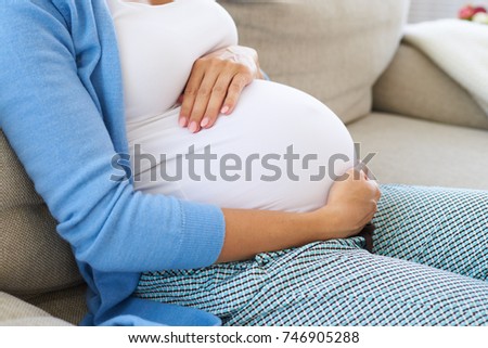 Side view of future mother sitting on sofa relaxing, touching tender her belly 