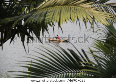 An African man fishing from his dugout canoe on Lake Kivu, Rwanda, viewed through palm fronds Royalty-Free Stock Photo #746907028