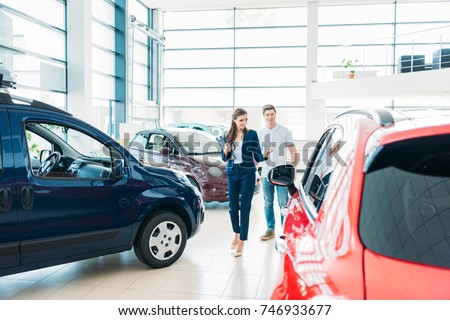 female sales manager showing red car to the customer in showroom Royalty-Free Stock Photo #746933677