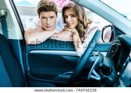 Boyfriend and girlfriend resting chins on hands on open car window in showroom