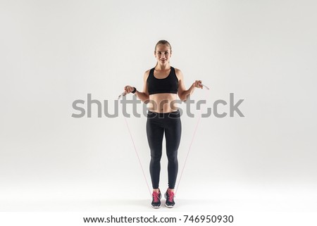 Happiness woman holding skipping rope, looking at camera and smiling. Studio shot, gray background