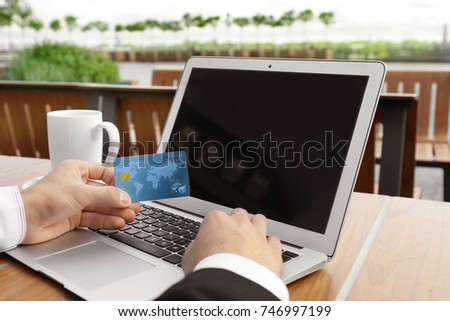 Young man using laptop and credit card for online shopping at table