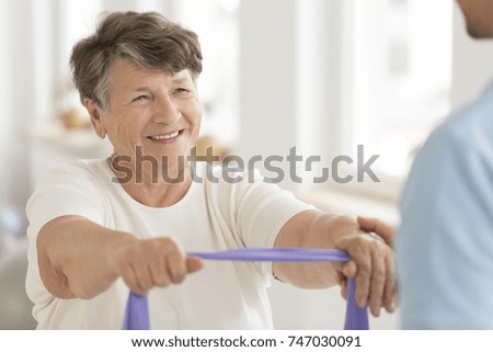 Smiling senior woman doing strength exercise with elastic band during fitness class