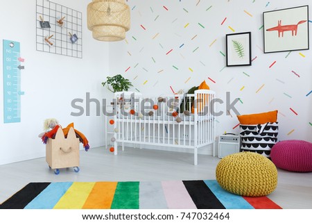 Colorful carpet in bright kid's bedroom with wooden box and yellow and pink pouf near cradle