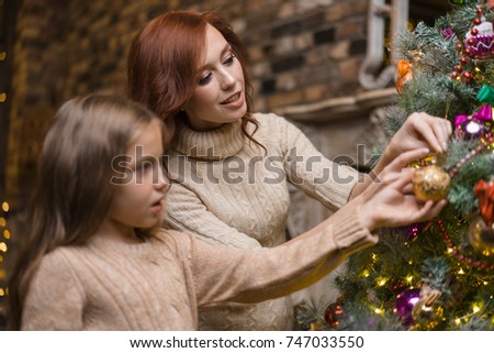 An attractive young woman with her little cute daughter decorating a Christmas tree