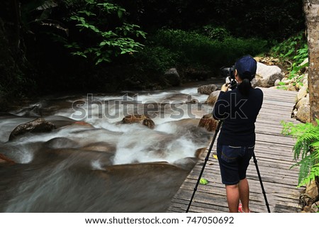 Young girl photographer taking picture of travel landscape Waterfall.Thailand nature photography with dslr camera on tripod at sunset with autumn background.