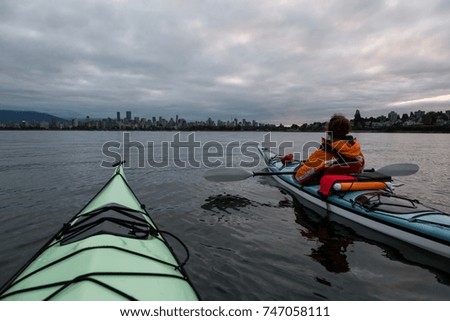 Adventurous girl is kayaking during a cloudy sunrise with city skyline in the background. Taken in Vancouver, British Columbia, Canada.
