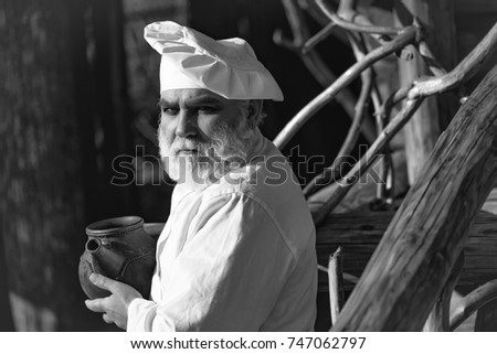 bearded man cook chef in uniform and hat with long beard on serious face holding iron old tea kettle sunny day outdoor on wooden background