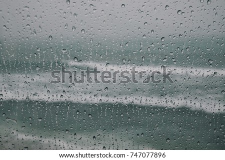 Drops of rain on window glass with the sea view background.