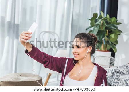 beautiful smiling young woman in earphones taking selfie with smartphone