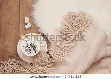Cozy Winter Mornings. Cappuccino and a warm scarf on a white fur carpet on the floor