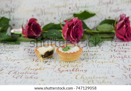 colorful christmas food photography image with seasonal iced mince pies red roses and leaves with sparkly glitter on petals with seasonal words in silver gold colors on wrapping paper background
