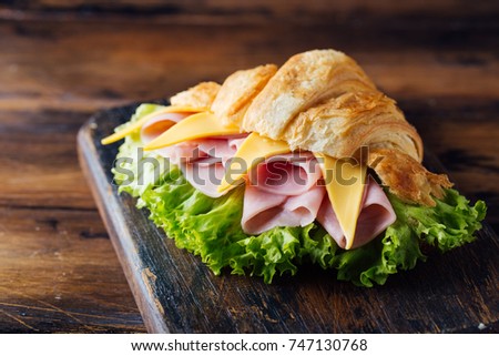 Sandwich croissant with ham and cheese on wooden board