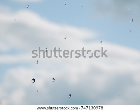 Rain water drops on glass on blue sky background