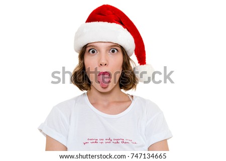 Photo of funny caucasian woman wearing christmas hat standing isolated. Looking camera showing tongue.