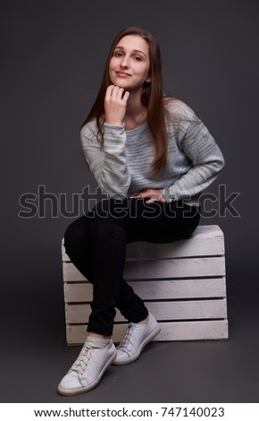 Portrait of charming girl in grey sweater siting on box who is posing and having fun