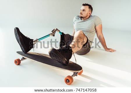 thoughtful young man with leg prosthesis with skateboard looking away isolated on white