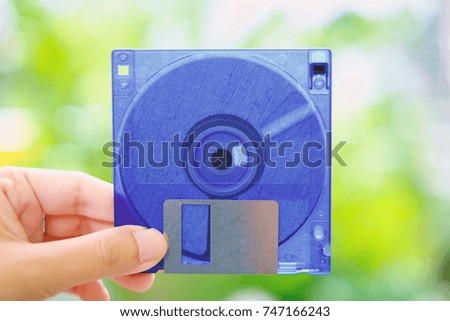 Hand holding a floppy disk against blurred background, old technology and legacy industrial computer equipment