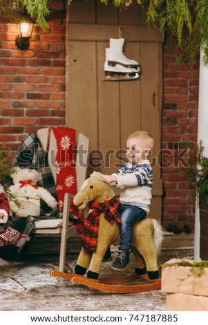 Playful smiling happy cute little child boy dressed in sweater and jeans sitting on rocking horse in decorated New Year room at home. Christmas good mood. Lifestyle, family and holiday 2018 concept