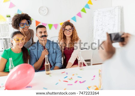 corporate, celebration and holidays concept - man taking picture of happy friends or team with party accessories having fun at office