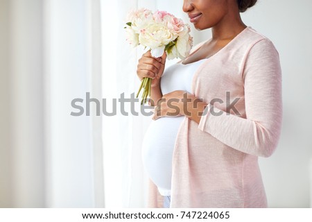 pregnancy, holidays and people concept - happy pregnant african american woman with flowers looking through window at home