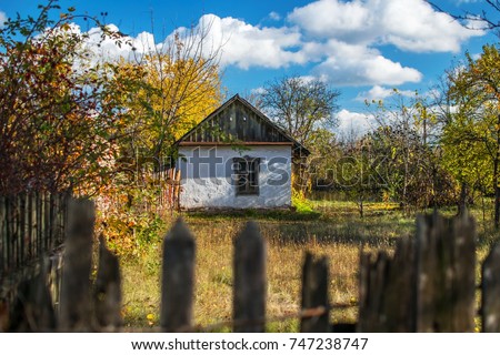 Old small white house fenced with an old wooden fence in the style of ancient Ukrainian traditions. Abandoned dwelling