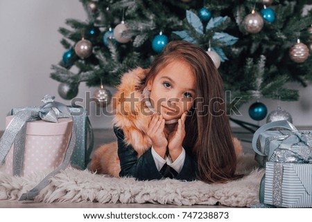 girl with dark hair lying on the carpet. Christmas tree in the background. smiles