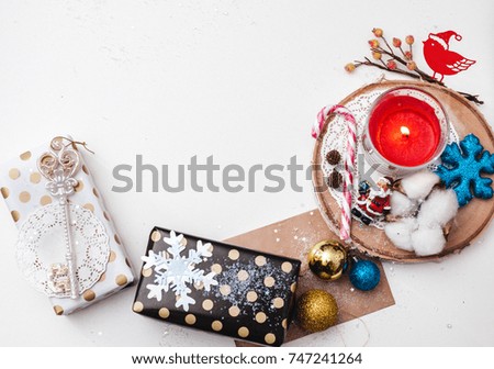 Flat lay concept of Christmas items on a white table. Composition includes decorations, gifts, tableware, candle, lace, cotton, tree, snow, glitter, letter balloons and the figure of Santa Claus.