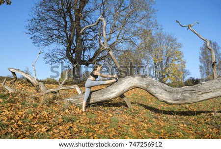 Young woman stretching her leg on tree in autumn nature. Sport, yoga.